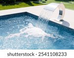 A modern swimming pool with a sleek water feature pouring water into the pool. The water is clear and blue, creating a refreshing atmosphere. The surrounding area is well-maintained with green grass.