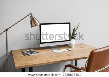 Modern table with computer, cup of coffee and houseplant near light wall