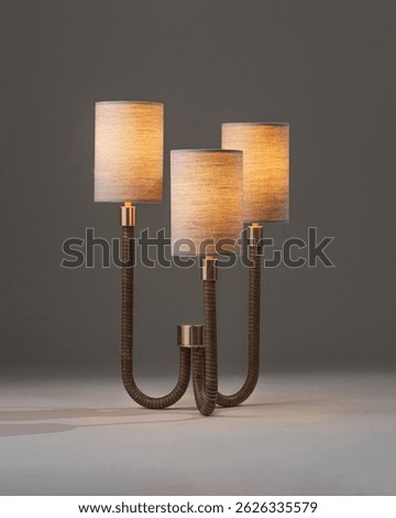 A modern table lamp with three cylindrical fabric lampshades supported by textured, curved metallic rods and gold accents on a flat surface.