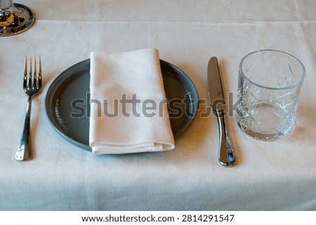 Modern table setting with ceramic plate folded white napkin knife fork and drinking glass viewed from above.