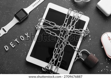 Modern tablet computer tied with chain, gadgets and word DETOX on dark background