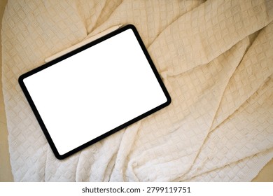 A modern tablet with an empty white screen and stylus rests on a soft cream knitted blanket, perfect for app UI mockup and technology lifestyle concepts.