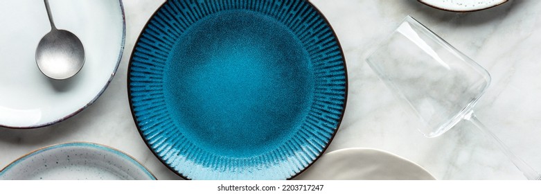 Modern Tableware Panorama With A Vibrant Blue Plate, Cutlery, And A Wine Glass, Overhead Flat Lay Shot. Trendy Dinnerware On A White Marble Table