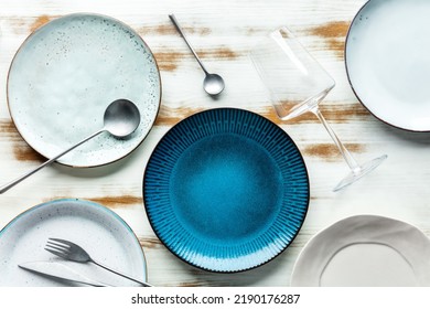 Modern tableware set with cutlery and a vibrant blue plate, with a glass for wine, overhead flat lay shot. Trendy dinnerware on a rustic background