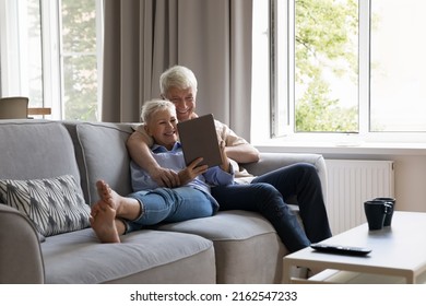 Modern tech for all ages. Bonding spouses retirees cuddle on couch at modern living room networking do shopping on electronic pad. Happy senior grandparents surf ecommerce websites on digital tablet - Powered by Shutterstock