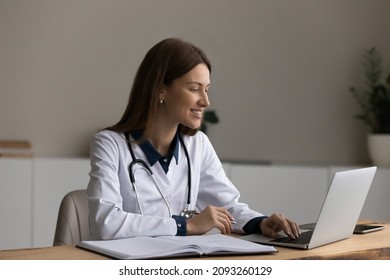 Modern Tech For Healthcare. Smiling Female Doctor Sit At Desk Use Laptop Watch Professional Training Webinar Online Manage Electronic Medical Document. Young Woman Gp Work On Computer In Clinic Office