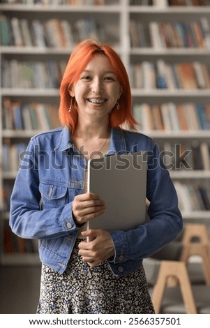 Modern tech and high school learning. Vertical portrait pretty cool looking red haired teen girl student showing pretty smile with brackets on teeth bringing notebook to library for effective studying