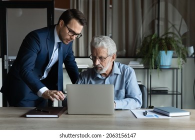 Modern tech in office. Skilled millennial ceo team leader explain work in corporate application on laptop to mature male colleague. Young man assist aged manager workmate in doing electronic paperwork