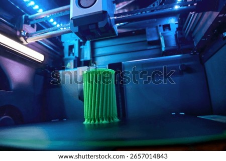 In a modern tech workshop, a 3D printer operates, meticulously crafting a vivid green object. The intricate design takes shape layer by layer, showcasing advanced printing technology.