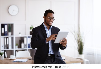 Modern technologies in business. Happy african american young businessman in suit using digital tablet in office, working online, reading marketing report, getting ready for presentation, copy space