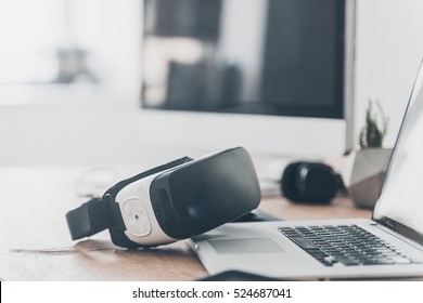 Modern technologies. Close-up of VR headset laying on the office desk and near laptop and computer