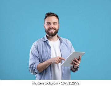 Modern technologies and communication. Portrait of happy bearded man using tablet computer over blue studio background. Young guy studying or working online on touch pad