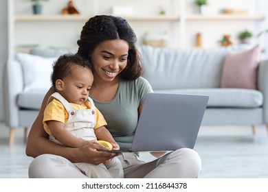 Modern Technologies Concept. Young Black Woman With Infant Baby Using Laptop At Home, Happy African American Mother Holding Her Toddler Son On Laps And Browsing Internet On Computer, Copy Space