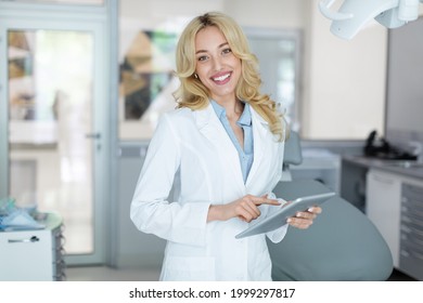 Modern technologies and healthcare concept. Pretty blonde lady dentist holding digital tablet and cheerfully smiling at camera, reading patient online medical card before treatment, copy space - Powered by Shutterstock