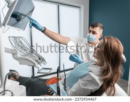 Modern technologies for installing dental implants allow patients to regain the natural appearance of a smile. Dentist showing screen to female patient in dental chair.