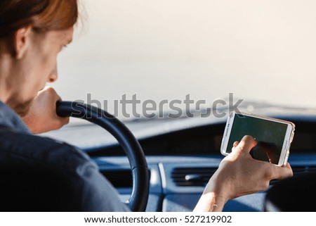 Modern technology concept. Man using mobile phone while driving car, checking social media or setting navigation.