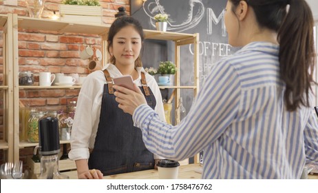 Modern Technology And People Concept. Female Bartender In Apron With Payment Terminal And Customer Hand With Smartphone At Bar Of Coffee Shop. Businesswoman Showing Waitress Mobile Phone Screen Pay