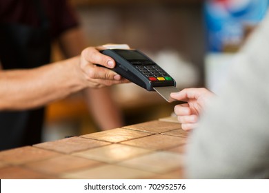 modern technology and people concept - man or bartender with payment terminal and customer hand with credit card at bar of coffee shop