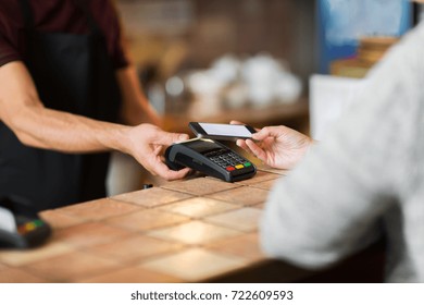 modern technology and people concept - man or bartender with payment terminal and customer with smartphone at bar of coffee shop