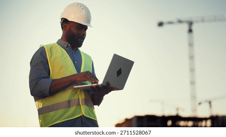 Modern technology and software for architect and builders, black man with laptop . Inspector or auditor checking quality of building, professional engineer on construction site, african ethnicity