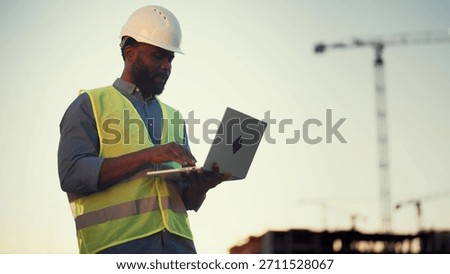 Modern technology and software for architect and builders, black man with laptop . Inspector or auditor checking quality of building, professional engineer on construction site, african ethnicity