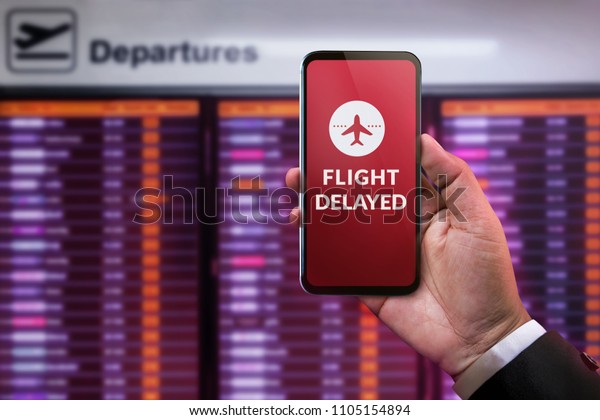 Modern\
Technology in Travel Concept. Flight Delayed on Smartphone Screen.\
Businessman using Mobile Phone in front of Departures Board to\
Re-Checked Flight Information in\
Airport