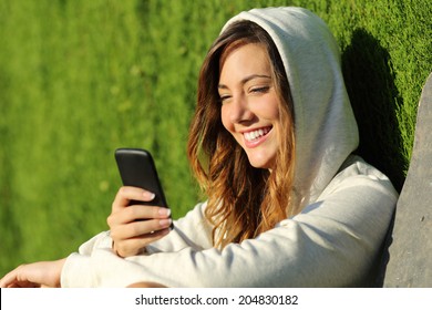 Modern Teenager Girl Using A Smart Phone In A Park With A Green Background               