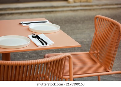 Modern Terrace Cafe, Restaurant On A Sidewalk Of A City Street. Peach Pink Retro Colors Chairs, Table With Served Dishes, Plates, Cutlery. Stylish Plastic Garden Furniture Outdoors. Fancy Exterior.