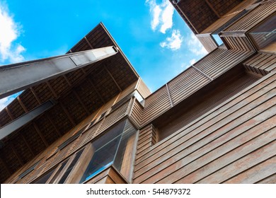 Modern timber clad building with an upward view to a cloudy blue sky