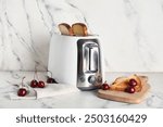 Modern toaster with bread slices and cherries on white marble background