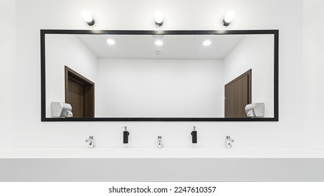 El wc es moderno y cuenta con un gran espejo iluminado. Gran lavabo con grifos para varias personas. El cuarto de baño es amplio y luminoso.