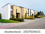 Modern townhouses in a residential area. New apartment buildings with green outdoor facilities in sustainable enviroment. Street  with Two-story townhouses. Townhouse along sidewalk with green lawn.