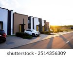 Modern townhouses in residential area. New apartment buildings in green in enviroment. Street  with Townhouse along sidewalk with green lawn. Car on parking lot at house. Townhouse in suburb. 