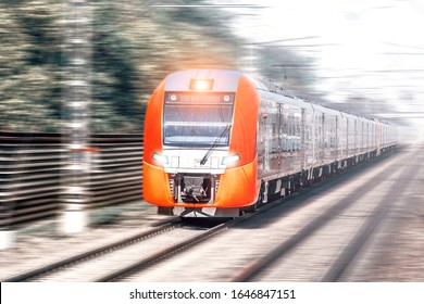 Modern Train In Motion On High Speed Transportation By Railway Blurred Landscape Against City Railroad Background. Front Wide View Of Red Intercity Train. Public Transport Concept