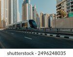 Modern tram navigating through pedestrian crosswalk bridge above promenade marina water with skyscrapers on the background