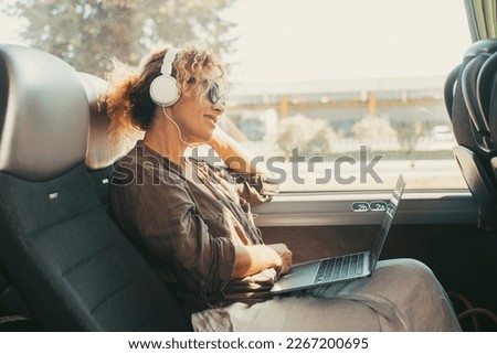 Modern travel lifestyle people with happy smiling woman listening music with headphones and laptop computer sitting and relaxing on a bus seat as a travel passenger. Transportation female people