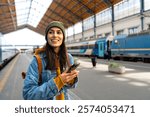 A modern traveller, a young woman with a backpack, using her smartphone to plan her next steps at the train station