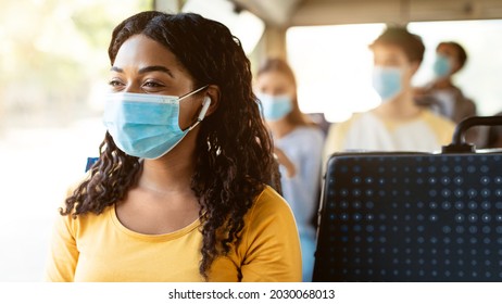 Modern Travels. Portrait Of Happy Smiling Black Female Passenger In Medical Face Mask Traveling On Public Transit, Listening To Music In Wireless Earphones Looking Away At Window, Thinking, Panorama