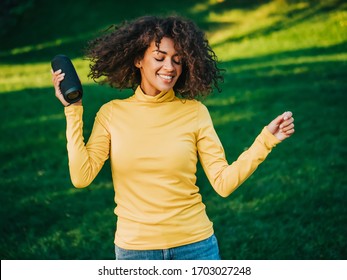 Modern Trendy African American Girl Listening To Music By Wireless Portable Speaker.Young Beautiful Woman Enjoying, Dancing In Park.