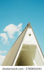 Modern triangular cabin architecture against a bright blue sky with minimalist design and geometric aesthetics.