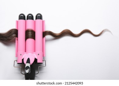 Modern triple curling iron with brown hair lock on white background, top view