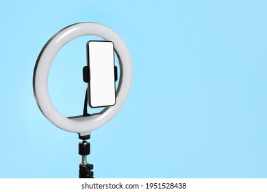 Modern Tripod With Ring Light And Smartphone On Light Blue Background. Space For Text