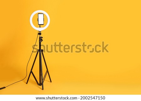 Modern tripod with ring light and smartphone on yellow background. Space for text