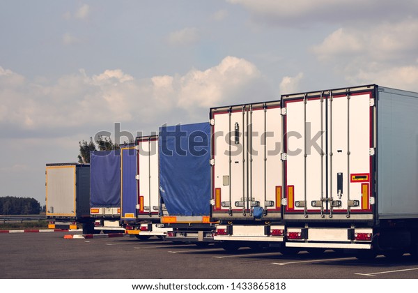 Modern trucks of various models are in a row on\
truck stop. Back view.