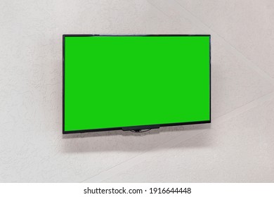 Modern TV Lcd Panel In Black Frame With Blank Green Mockup Screen Hangs On White Empty Wall