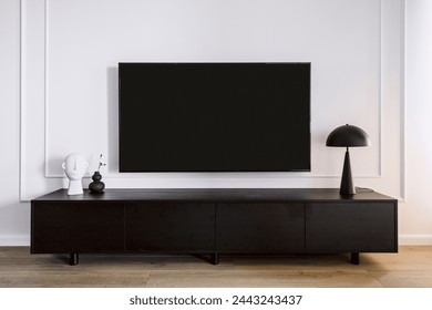 Modern tv screen hanging on white wall in living room with minimalistic interior. Black wooden stand under device. Home decor and lamp on cabinet. Household electronics concept - Powered by Shutterstock