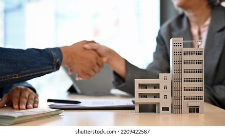 Modern urban building or condominium model on the table with a blurred background of two businesspeople shaking hands. real estate agent concept