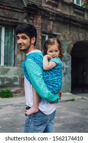 Modern Urban Family Baby Wearing Concept With Father Carry Baby Toddler Girl In Blue Fabric Wrap Carrier Sling Scarf At City Background, Casual Look Barefoot Child