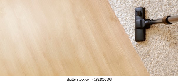 Modern vacuum cleaner on a beige carpet on a background wooden light coloured parquet. Concept of housekeeping, housework, vacuuming the carpet. 
Long banner wiht copy space for text. Top view.