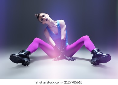 Modern vanguard fashion. A gorgeous model girl in bright extravagant clothes posing on the floor. Gray studio background. Black makeup and avant-garde hairstyle.